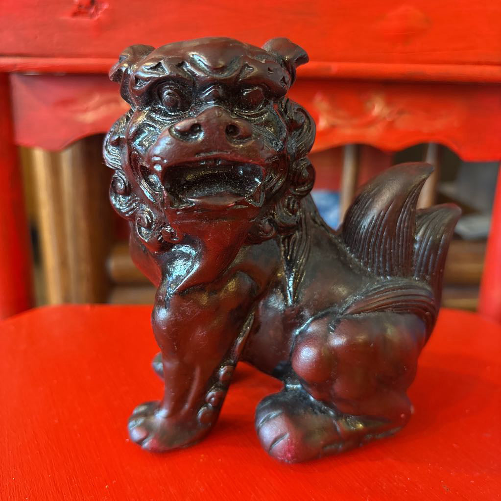 Mahogany colored foo dog figurine on a red surface. 
