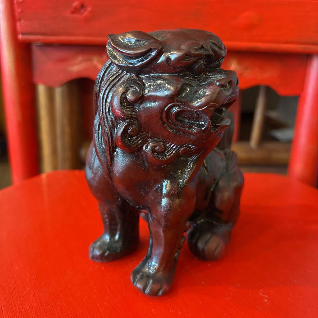 Mahogany colored foo dog figurine on a red surface. 
