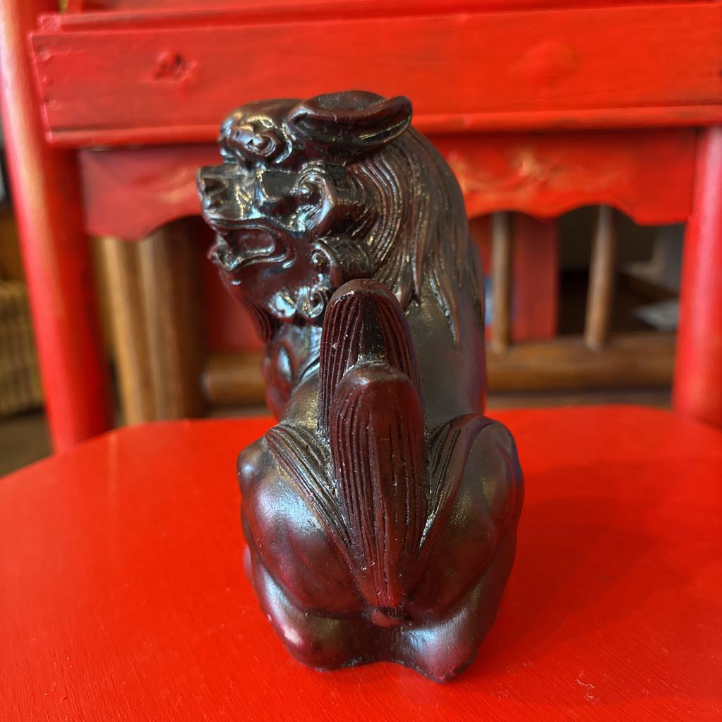 Mahogany colored foo dog figurine on a red surface. 