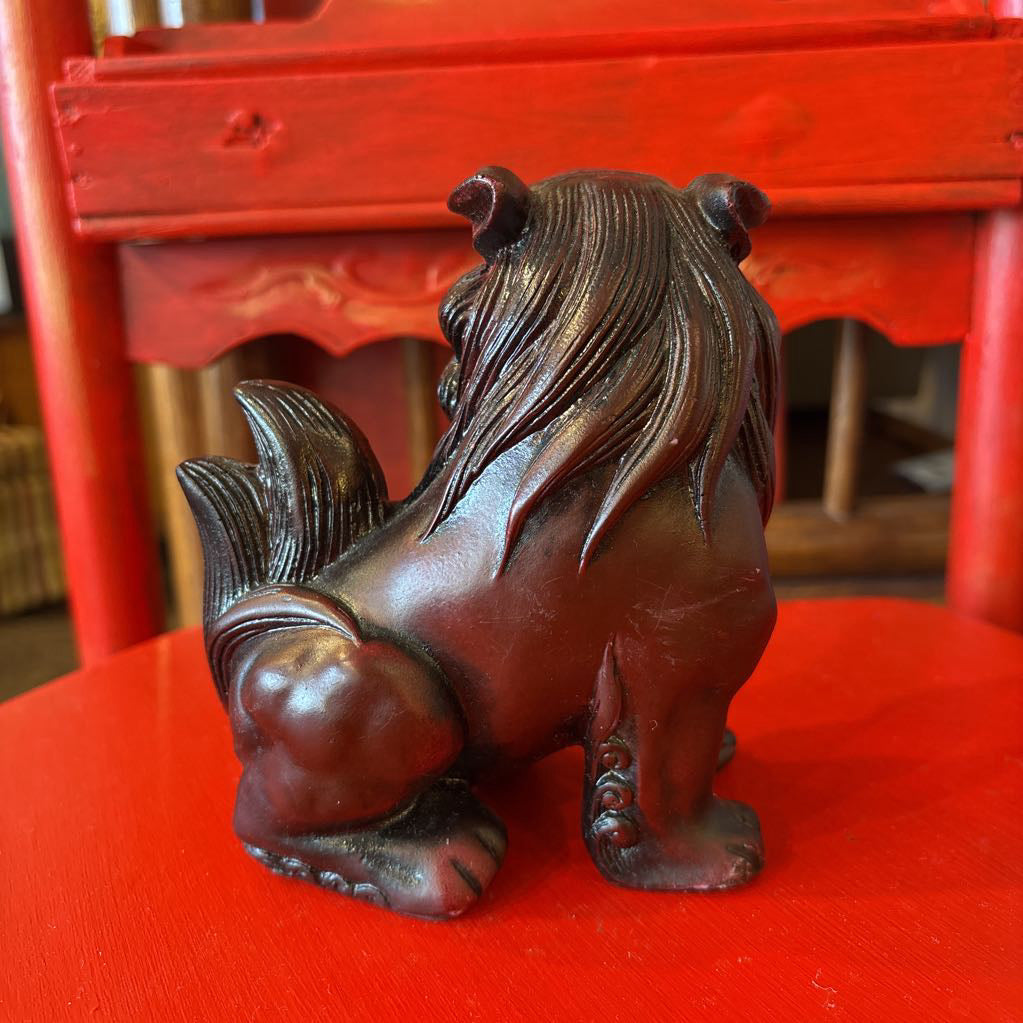 Mahogany colored foo dog figurine on a red surface. 