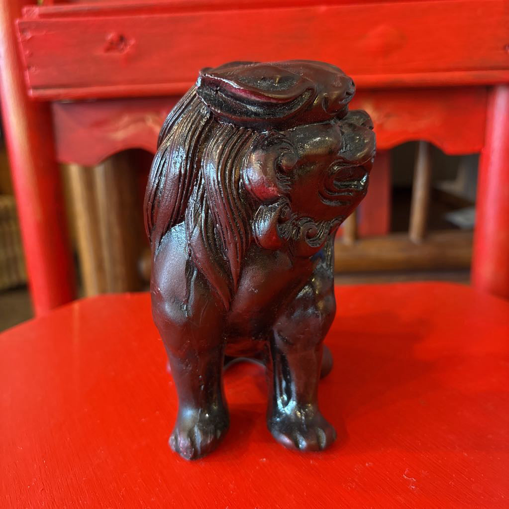 Mahogany colored foo dog figurine on a red surface. 