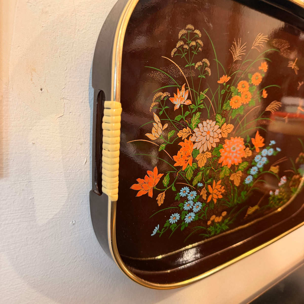 A brown tray with a floral design on a white wall.