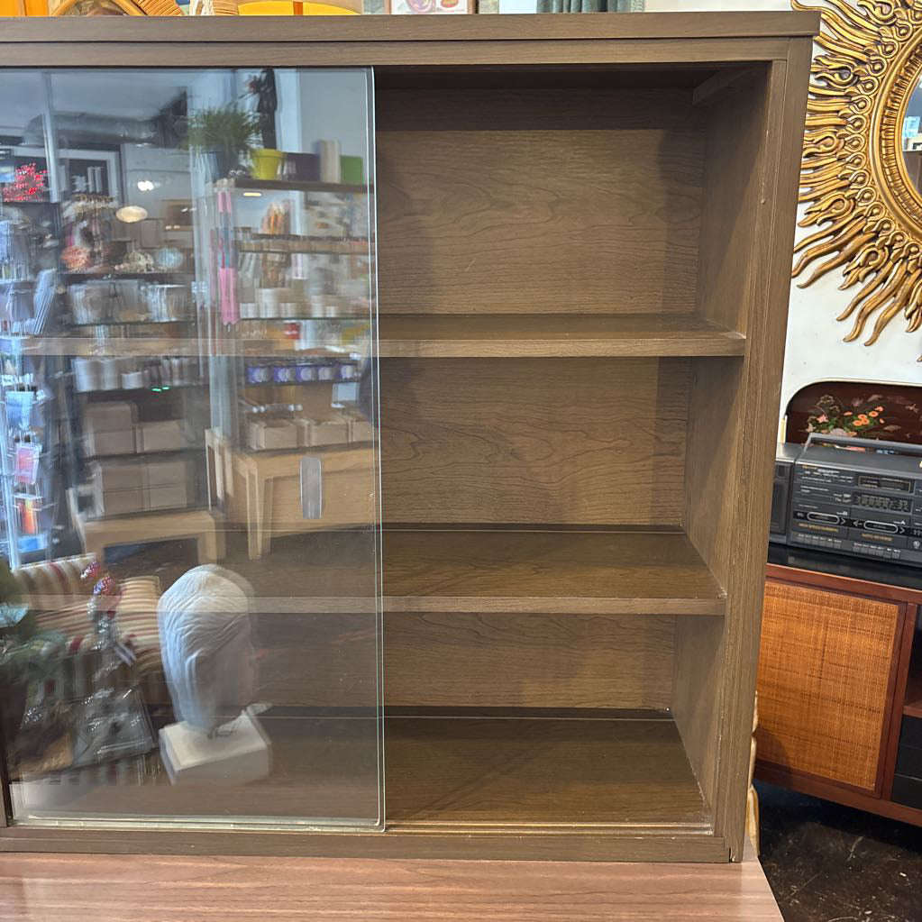 A large wooden hutch with two sliding glass doors. The cabinet is in a store setting. 