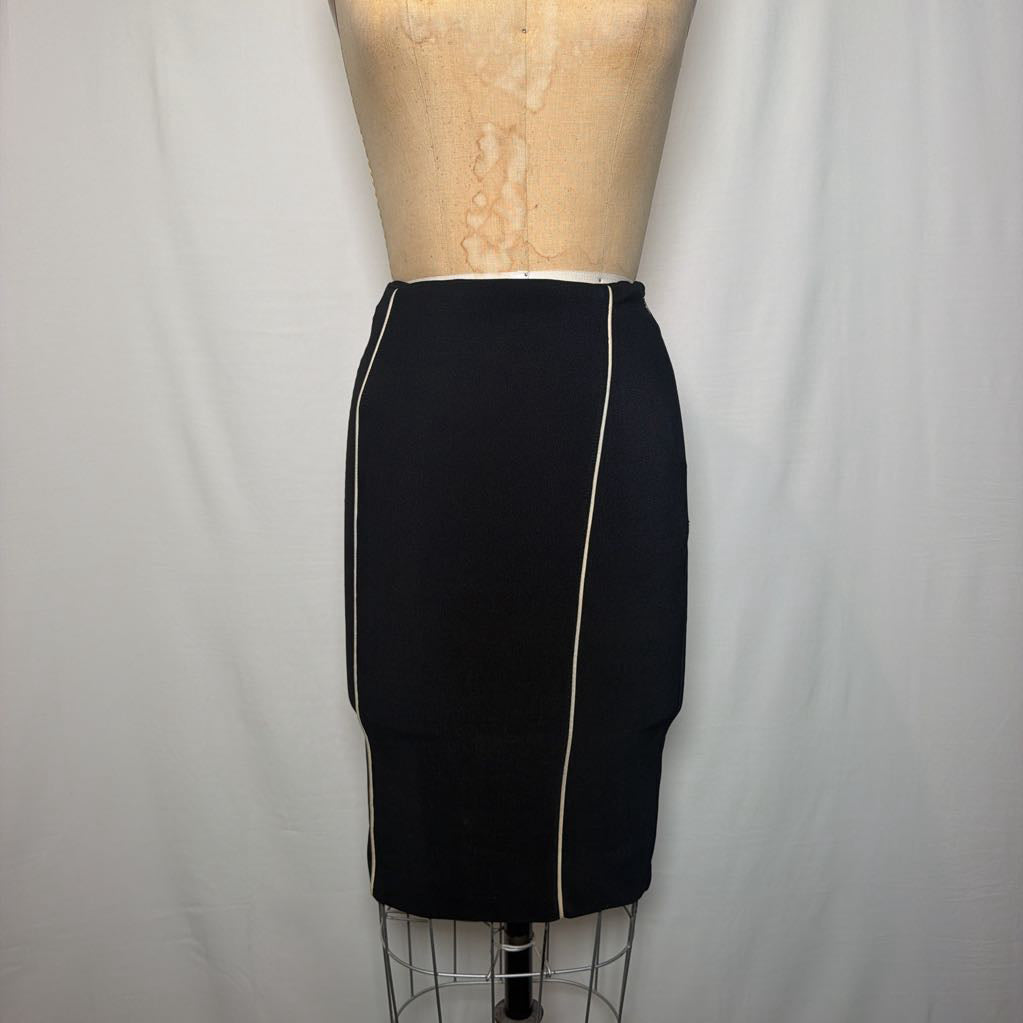 A black pencil skirt with white lines down the front and side on an antique mannequin in front of a white fabric wall. 