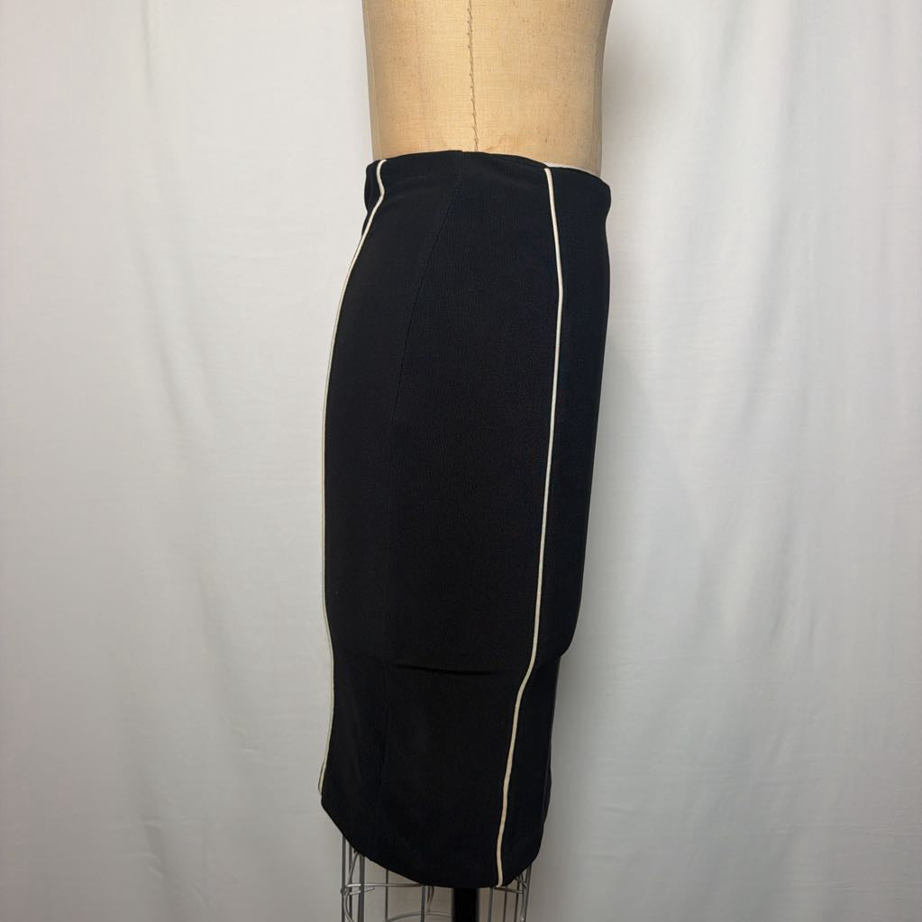 A black pencil skirt with white lines down the front and side on an antique mannequin in front of a white fabric wall. 