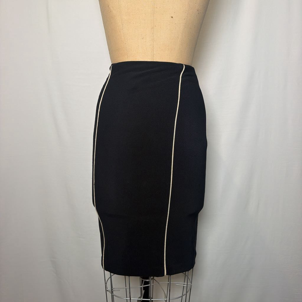 A black pencil skirt with white lines down the front and side on an antique mannequin in front of a white fabric wall. 