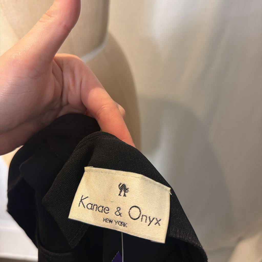 A hand holding a "Kanae & Onyx New York" brand tag in front of a white wall.