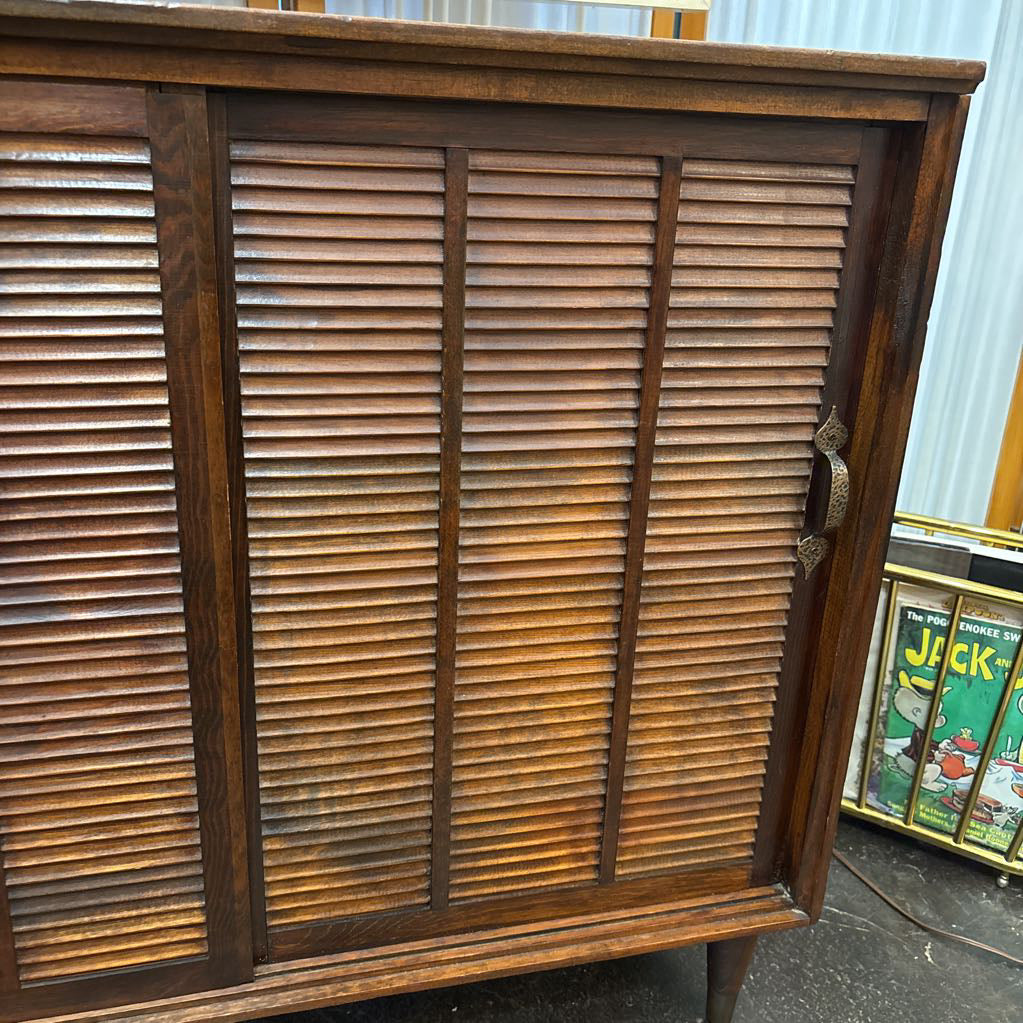 A mid-century modern wooden cabinet with three doors featuring horizontal louvered slats, finished in a warm medium-to-dark brown wood tone with a dark metal pull handle.