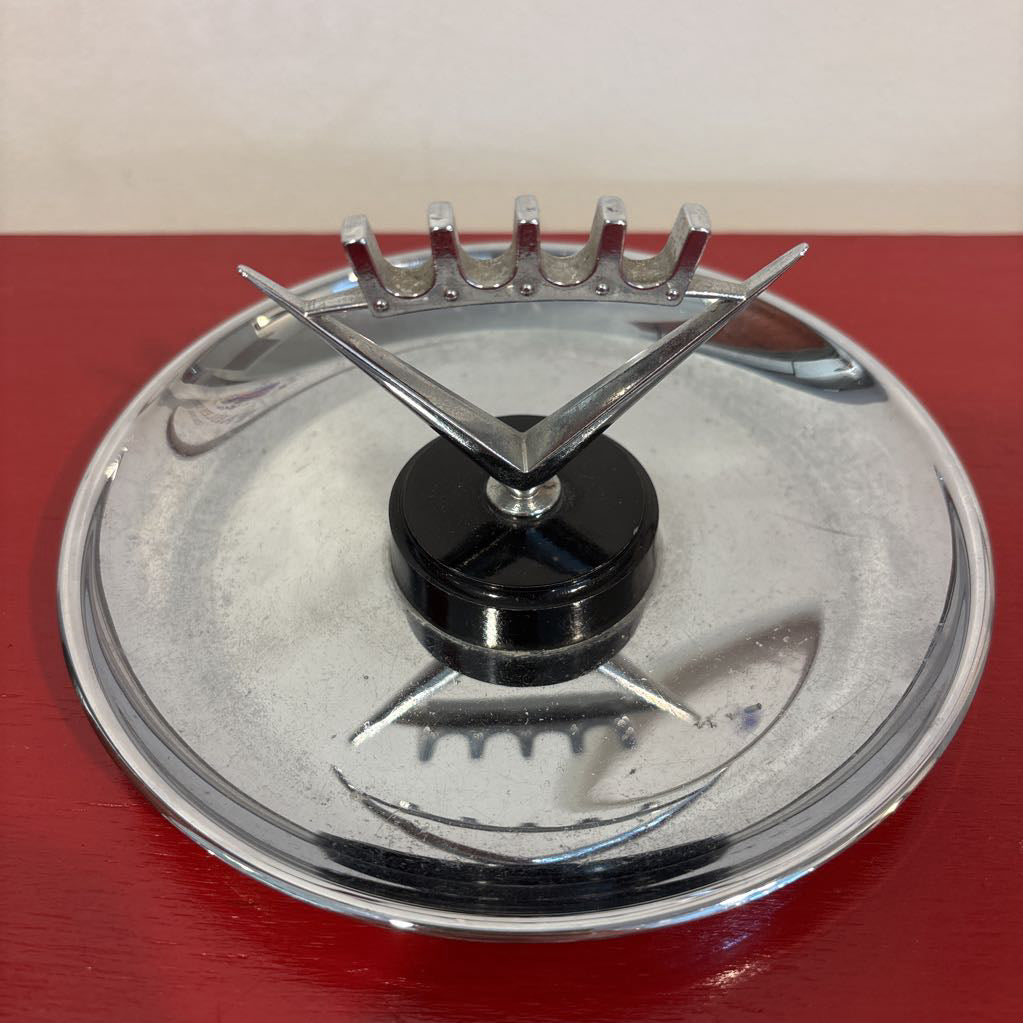 A mid-century style chrome ashtray dish on a red surface and up against a white wall. 