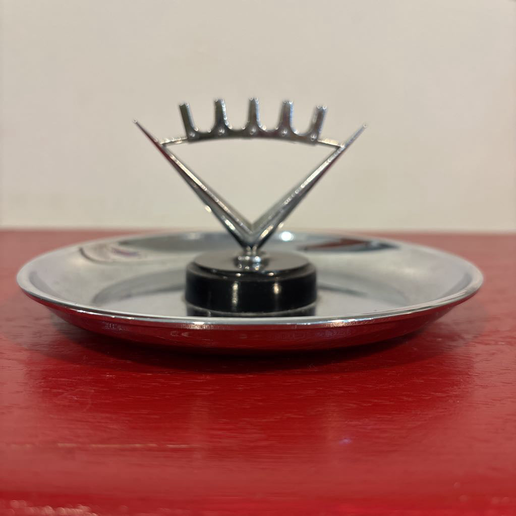 A mid-century style chrome ashtray dish on a red surface and up against a white wall. 