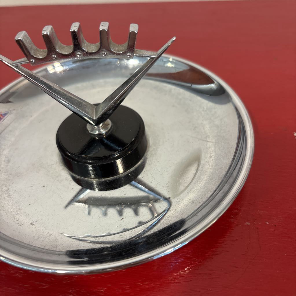 A mid-century style chrome ashtray dish on a red surface and up against a white wall. 