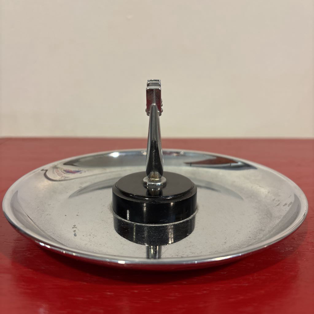 A mid-century style chrome ashtray dish on a red surface and up against a white wall. 