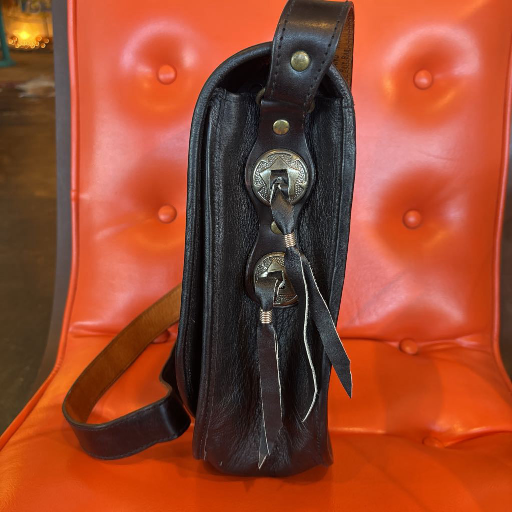 A black leather belt bag with silver hardware. This bag sits on an orange cushion in a room setting.