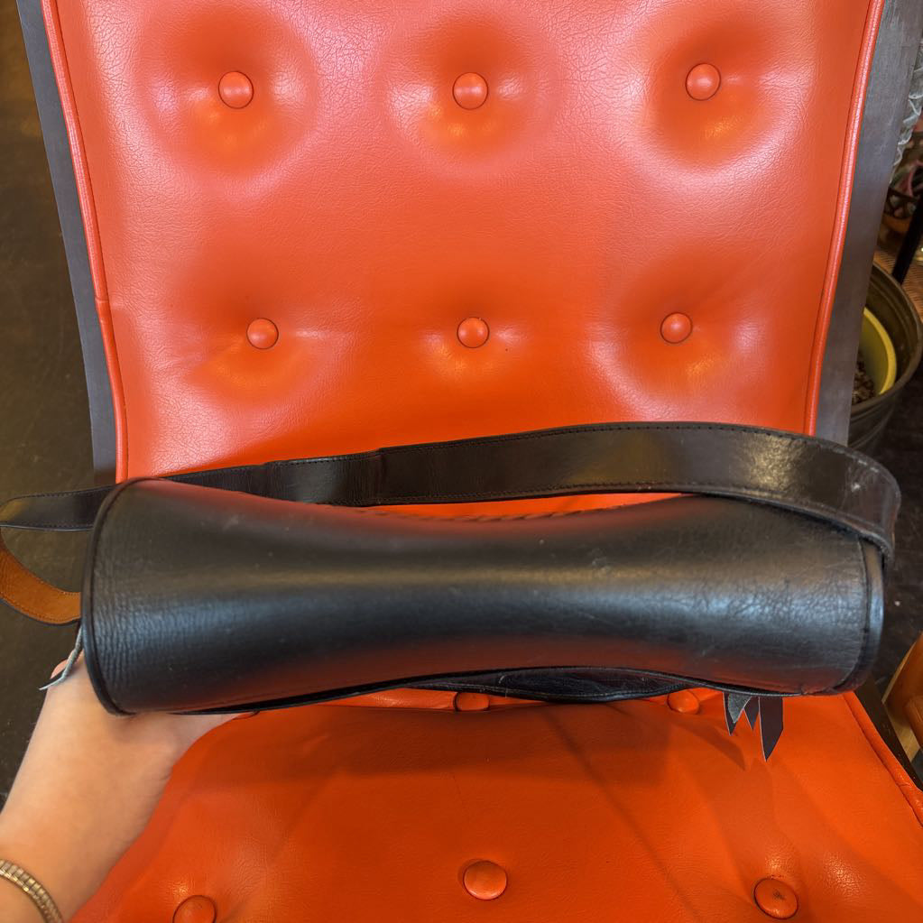 A black leather belt bag on an orange cushion in a room setting.