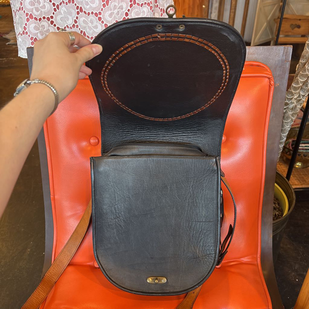 A black leather belt bag on an orange cushion in a room setting.