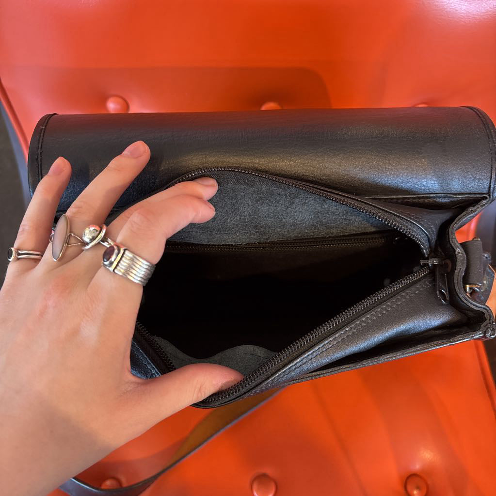 A black leather belt bag on an orange cushion in a room setting.