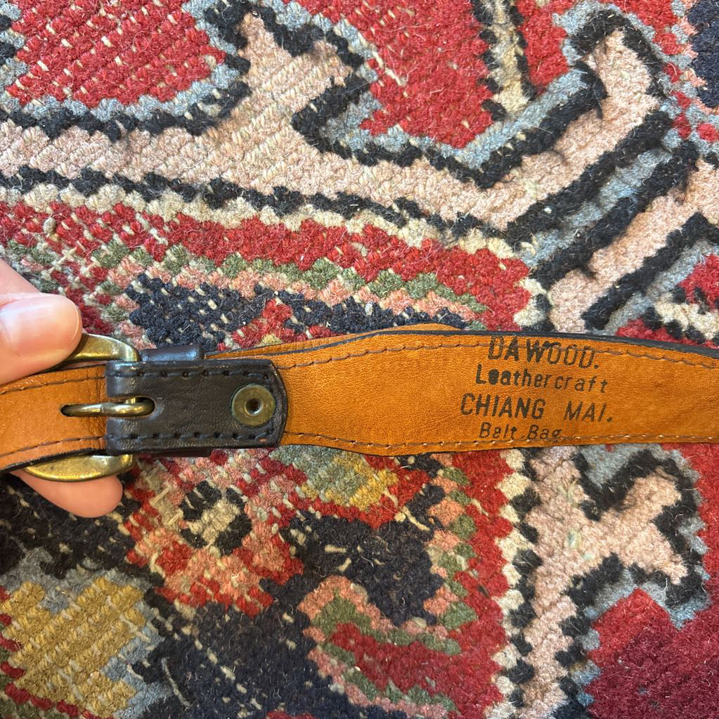 A black leather belt bag with a Native American figure's profile embossed in a circular design on the front. This bag sits on a decorative rug. 