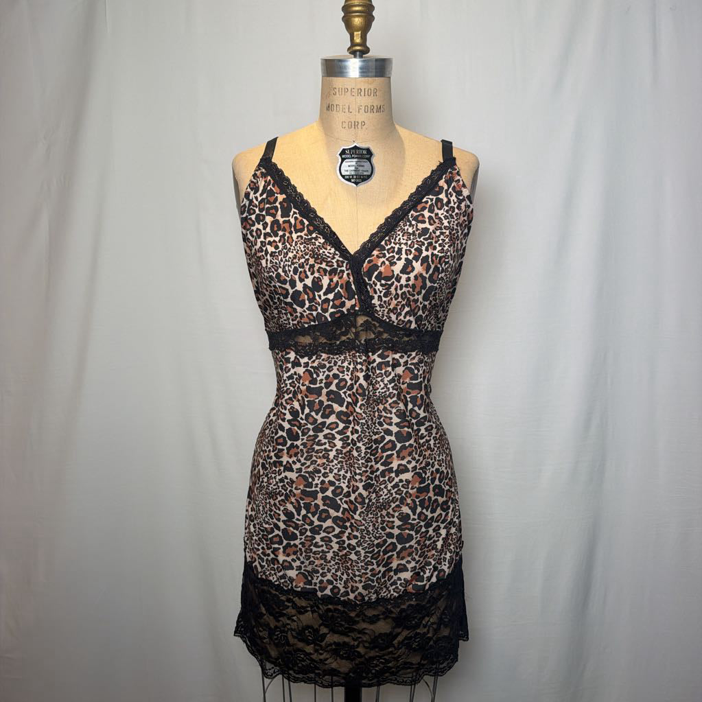 A leopard print lingerie slip dress with black lace trimmings on an antique style mannequin in front of a white fabric wall. 