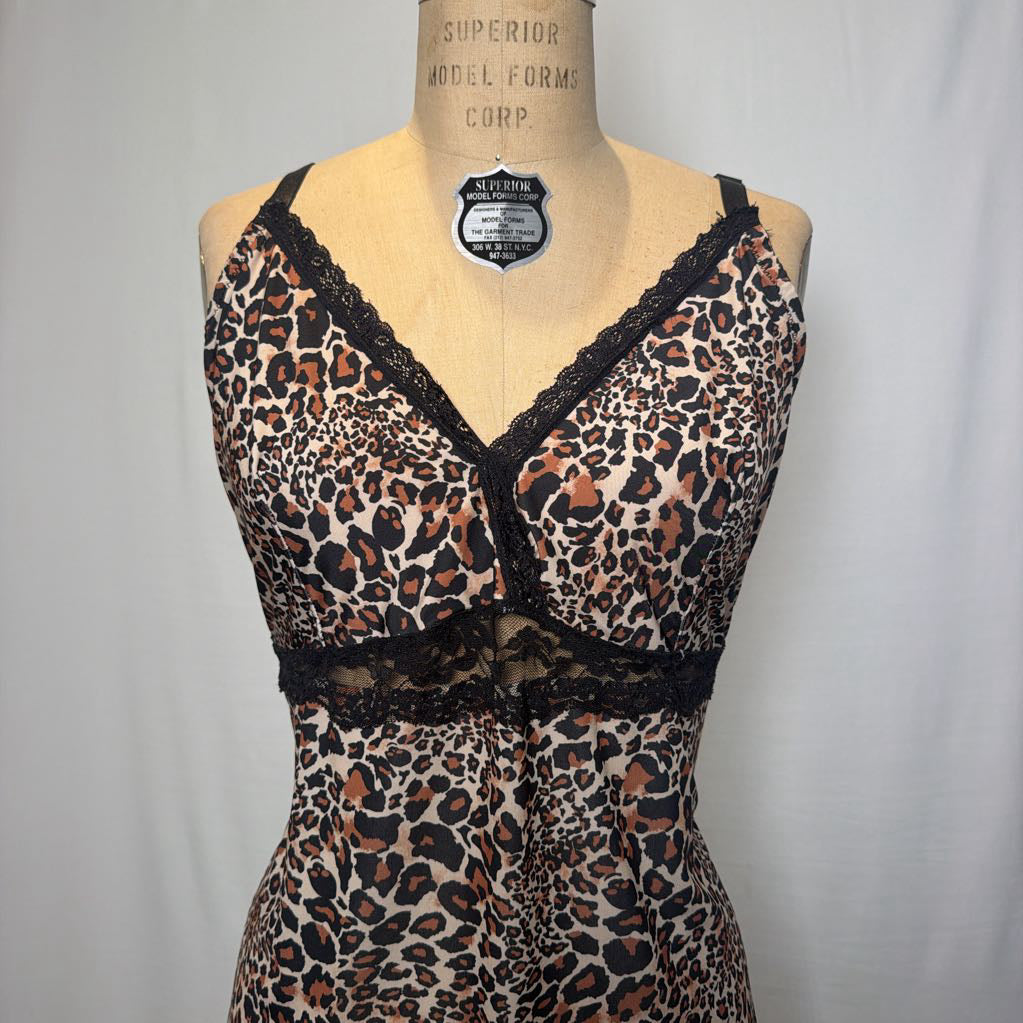 A leopard print lingerie slip dress with black lace trimmings on an antique style mannequin in front of a white fabric wall. 