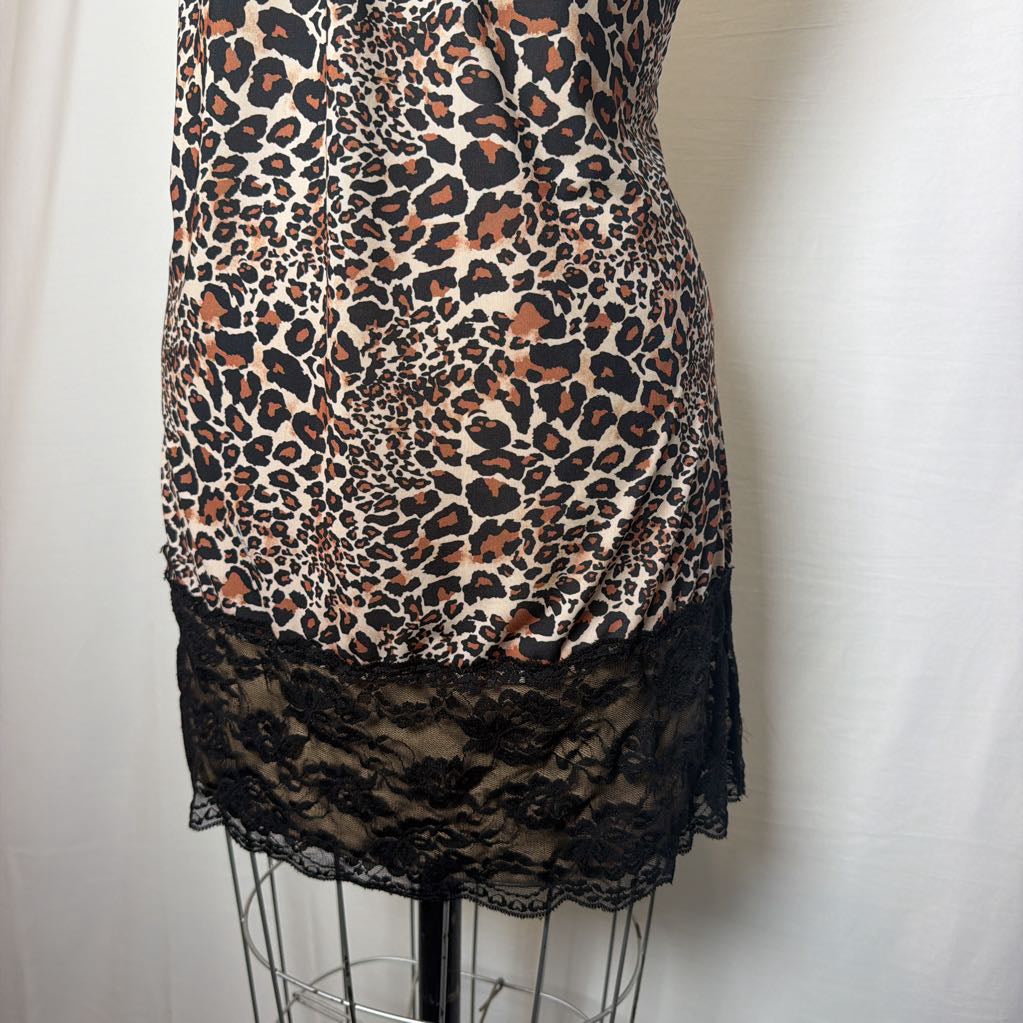 A leopard print lingerie slip dress with black lace trimmings on an antique style mannequin in front of a white fabric wall. 