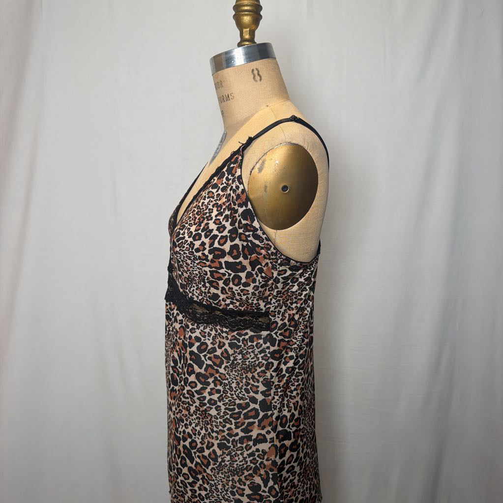 A leopard print lingerie slip dress with black lace trimmings on an antique style mannequin in front of a white fabric wall. 