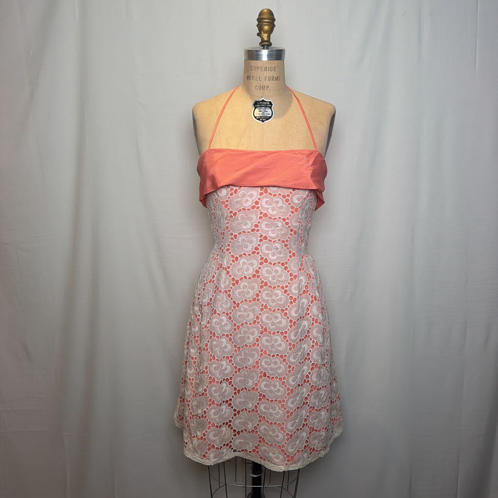 A peach and white lace halter mini dress on an antique style mannequin, against a white fabric wall. 