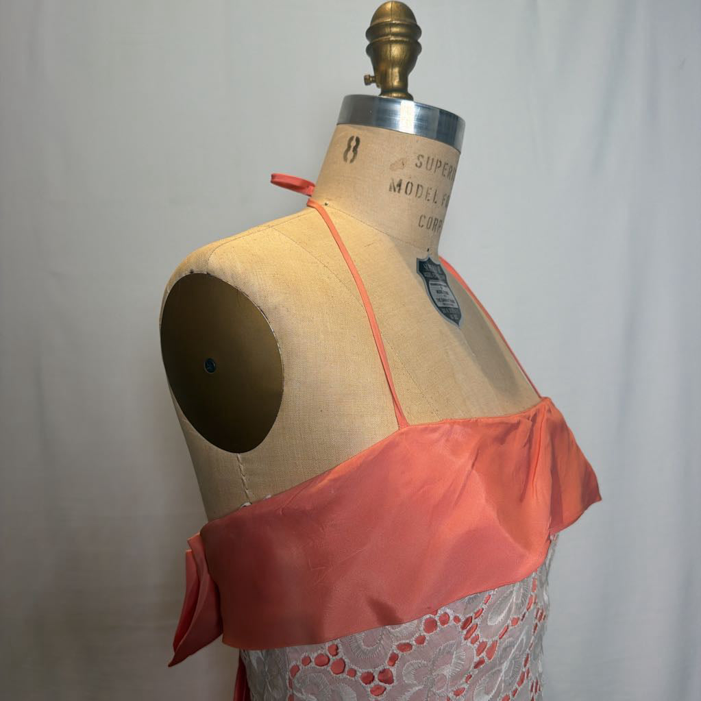 A peach and white lace halter mini dress on an antique style mannequin, against a white fabric wall. 