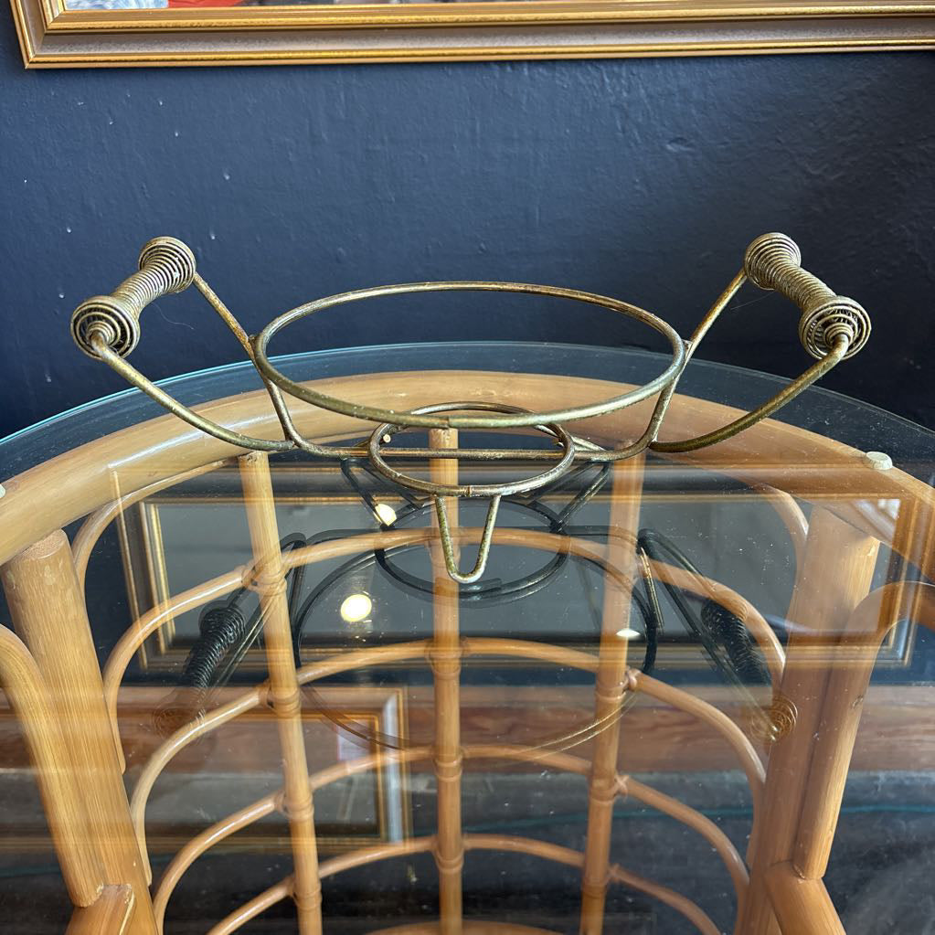 A ceramic turquoise serving bowl and lid in a brass wire caddy with handles on a glass table in front of a black wall.