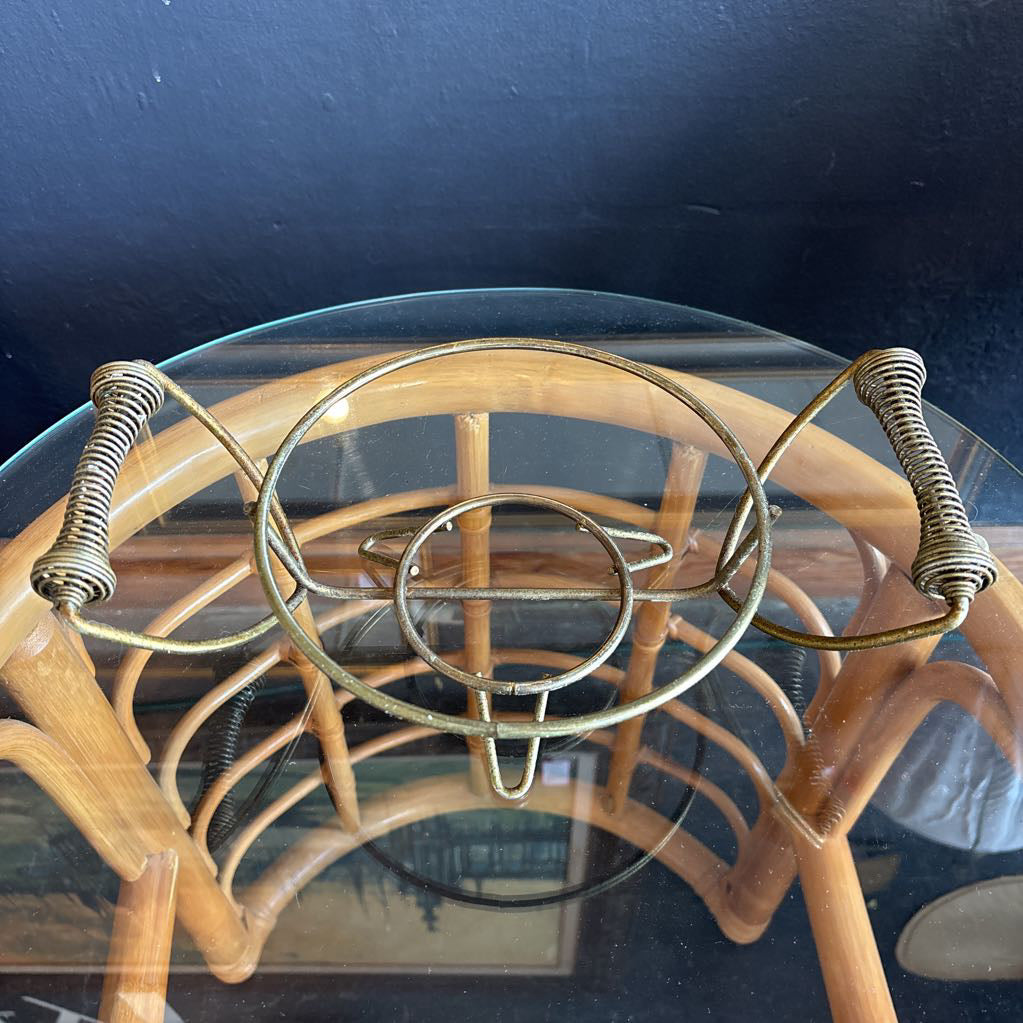 A ceramic turquoise serving bowl and lid in a brass wire caddy with handles on a glass table in front of a black wall.