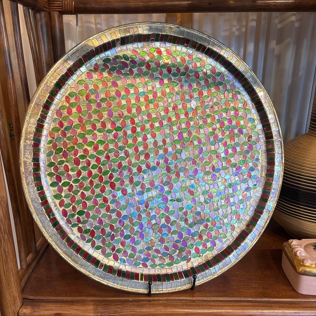 A large tray with a glass mosaic design on  a wooden shelf.