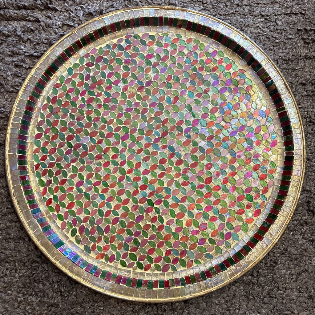A large tray with a glass mosaic design on a brown rug. 