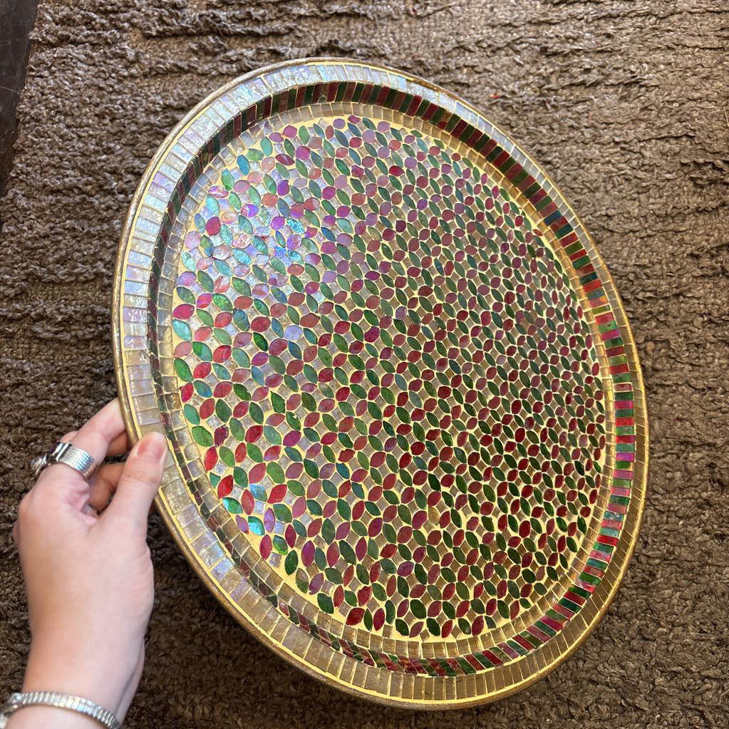 A large tray with a glass mosaic design on a brown rug. 
