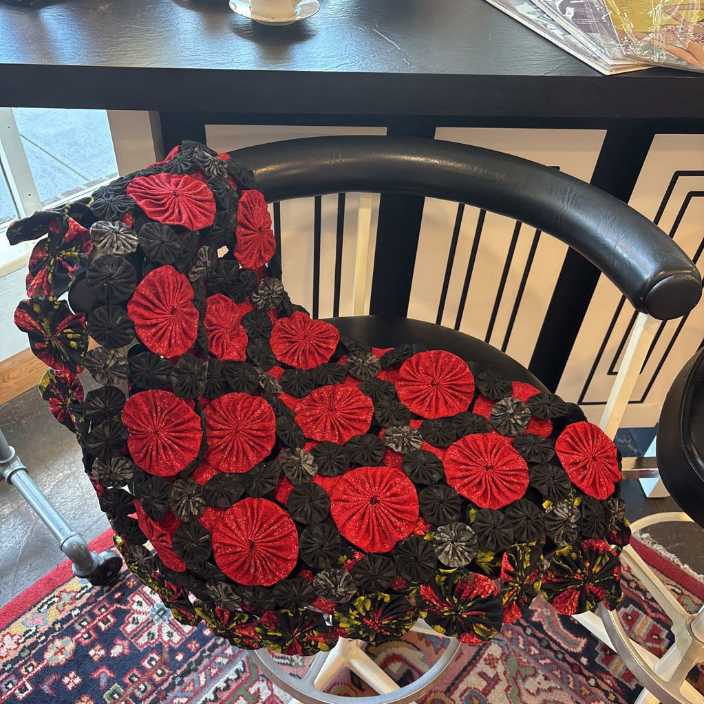A red and black puff quilt laid over a black chair against a black and white bar.