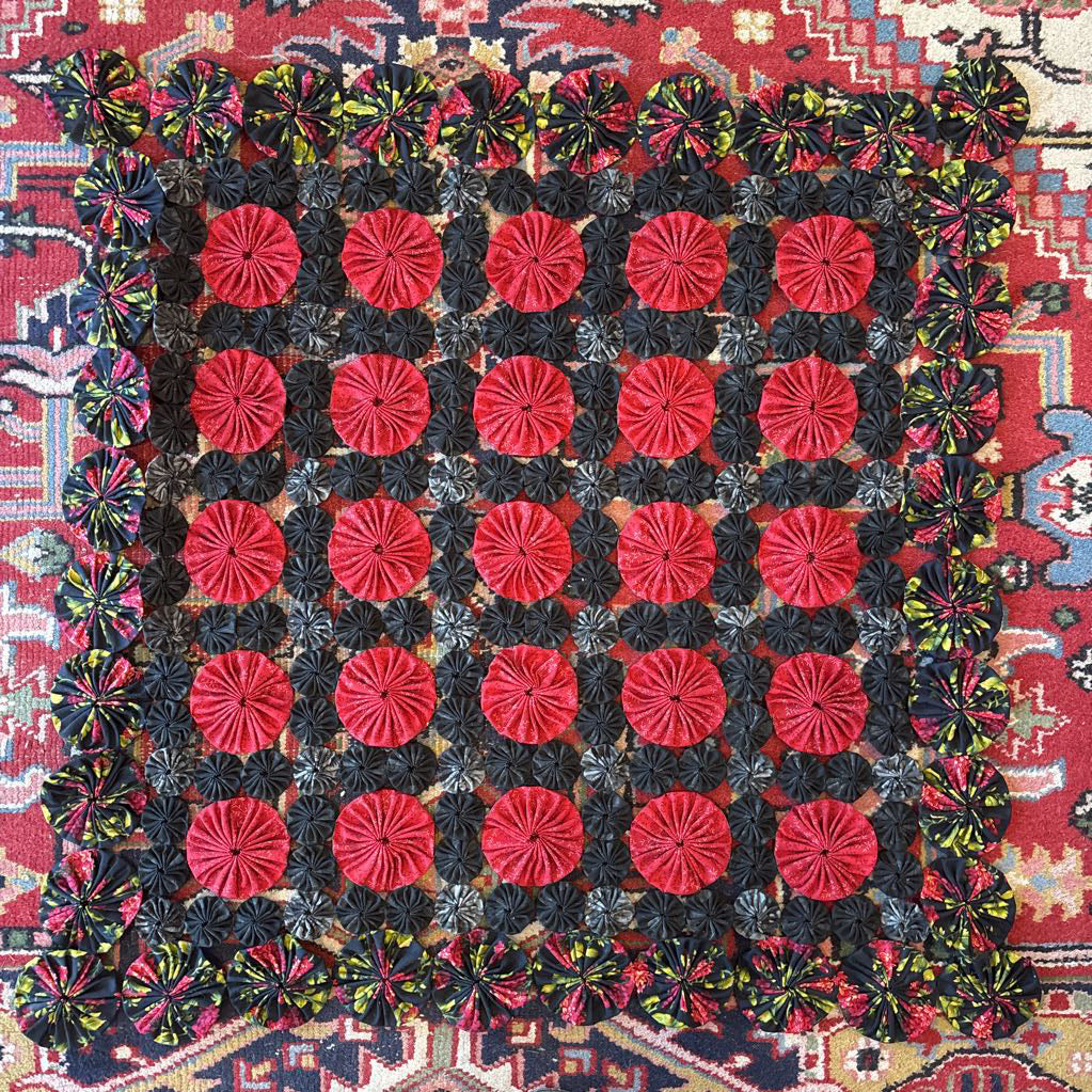 A red and black puff quilt on a red rug.