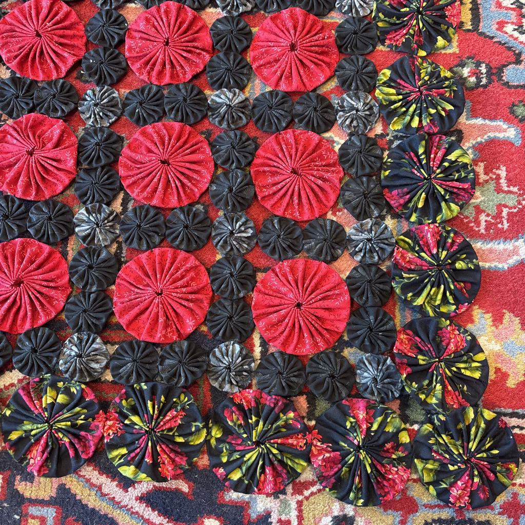 A red and black puff quilt on a red rug.