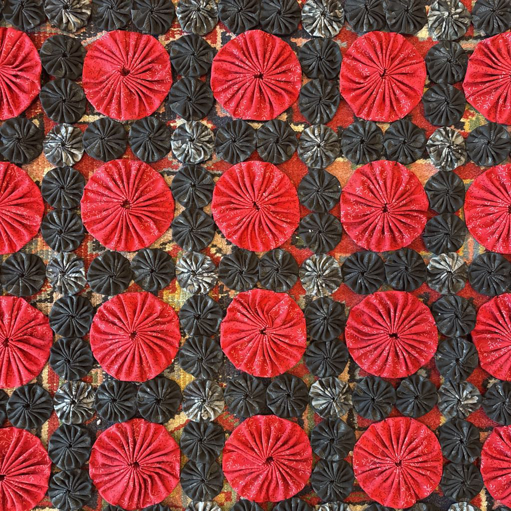 A red and black puff quilt on a red rug.