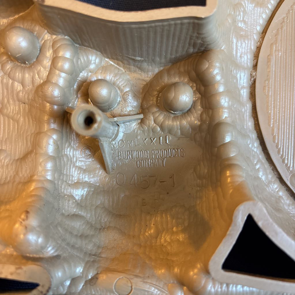 A vintage clock of 3 owls with wide eyes sitting on a branch and the clock face in the largest owl. This clock is on a blue cushion. 