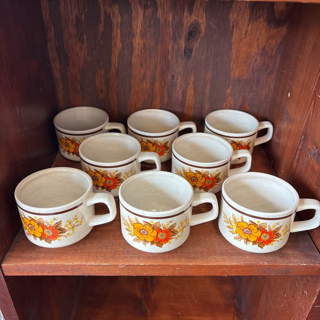 White ceramic mugs with floral designs in a wooden cabinet.
