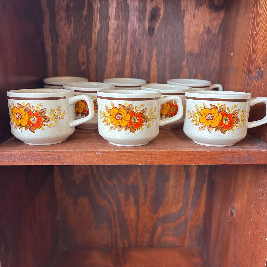 White ceramic mugs with floral designs in a wooden cabinet.