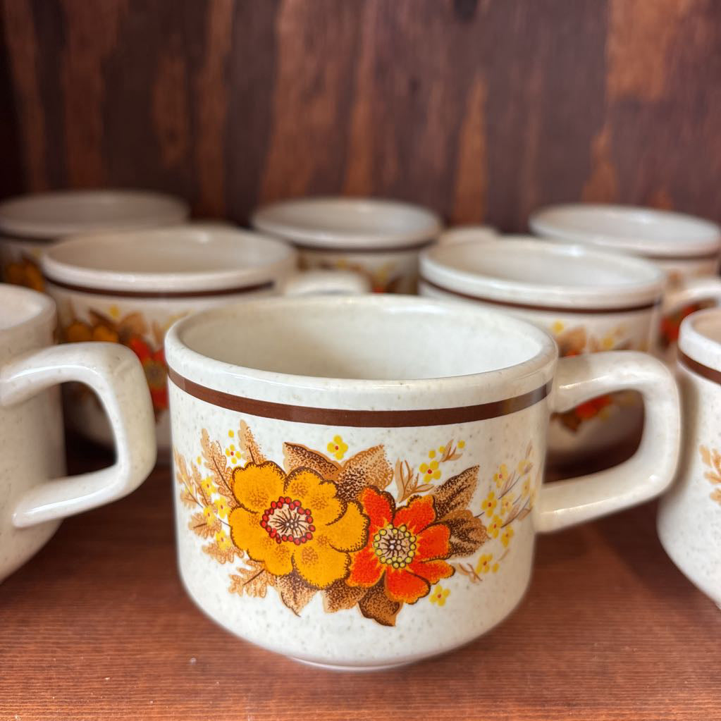 White ceramic mugs with floral designs in a wooden cabinet.