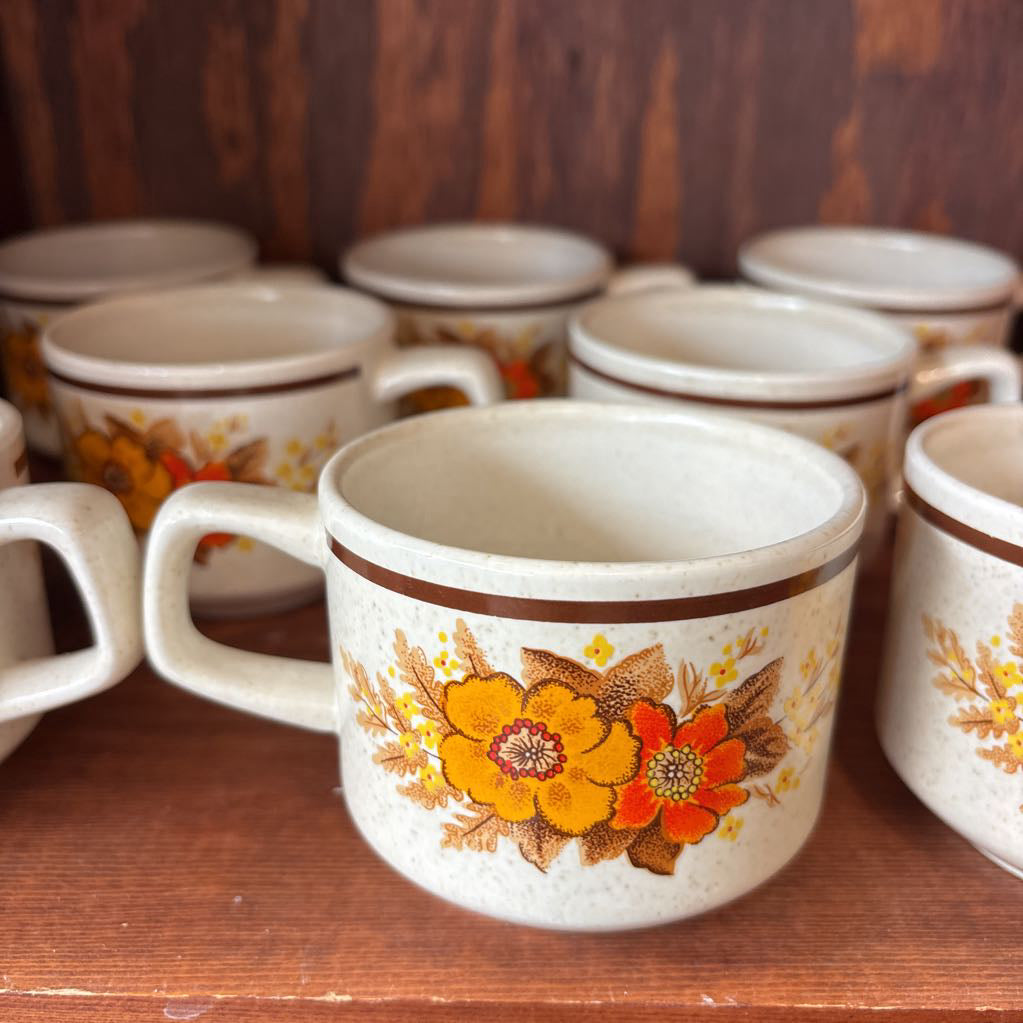 White ceramic mugs with floral designs in a wooden cabinet.