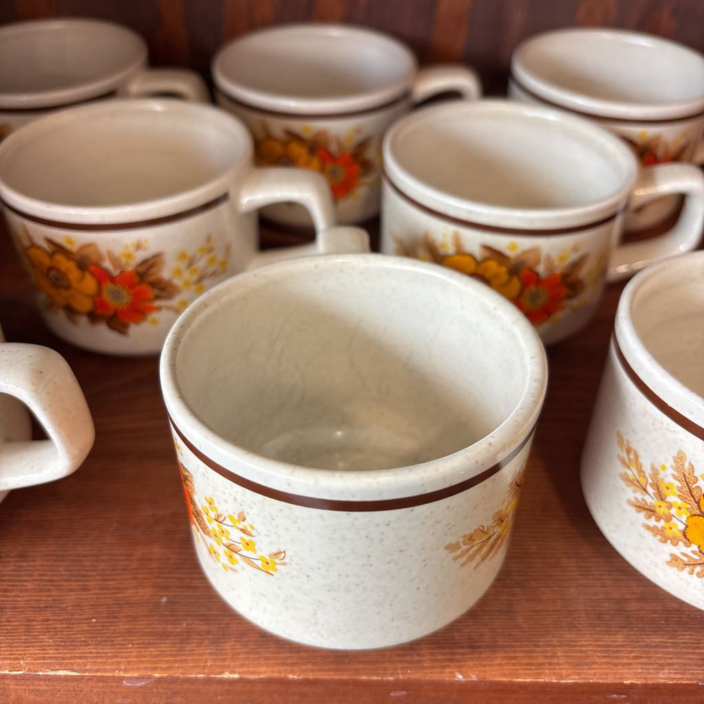 White ceramic mugs with floral designs in a wooden cabinet.