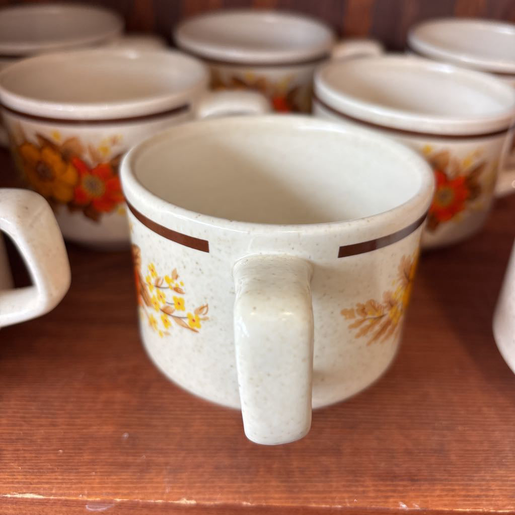 White ceramic mugs with floral designs in a wooden cabinet.