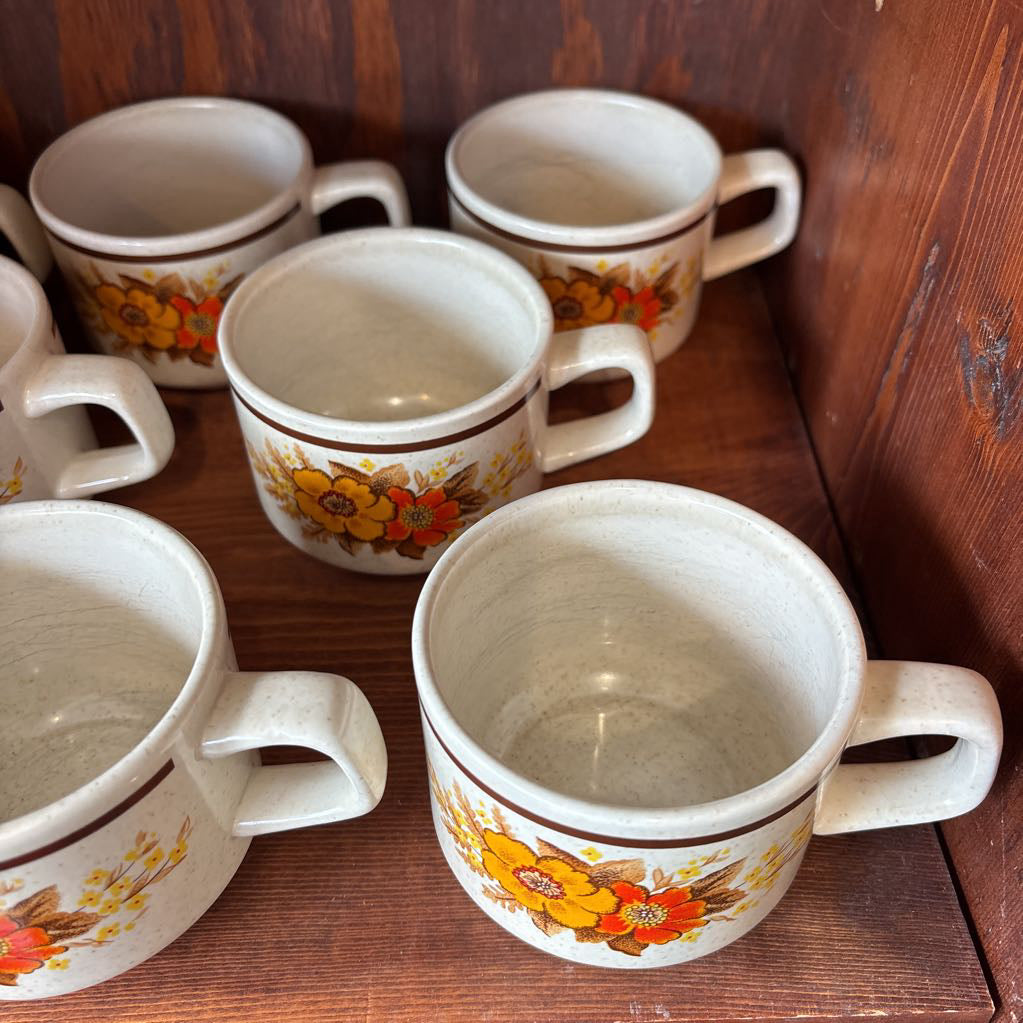 White ceramic mugs with floral designs in a wooden cabinet.