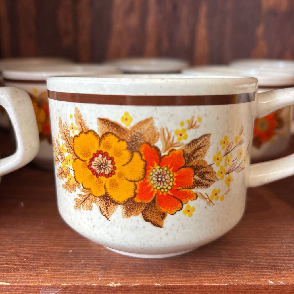White ceramic mugs with floral designs in a wooden cabinet.