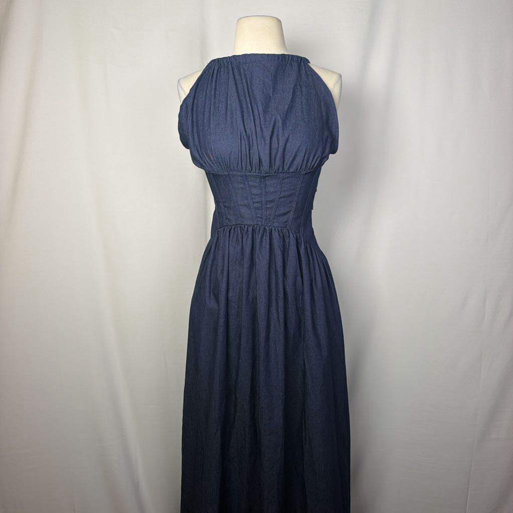 A sleeveless halter-neck maxi dress in dark blue chambray fabric, displayed on a cream mannequin torso against a white fabric backdrop.