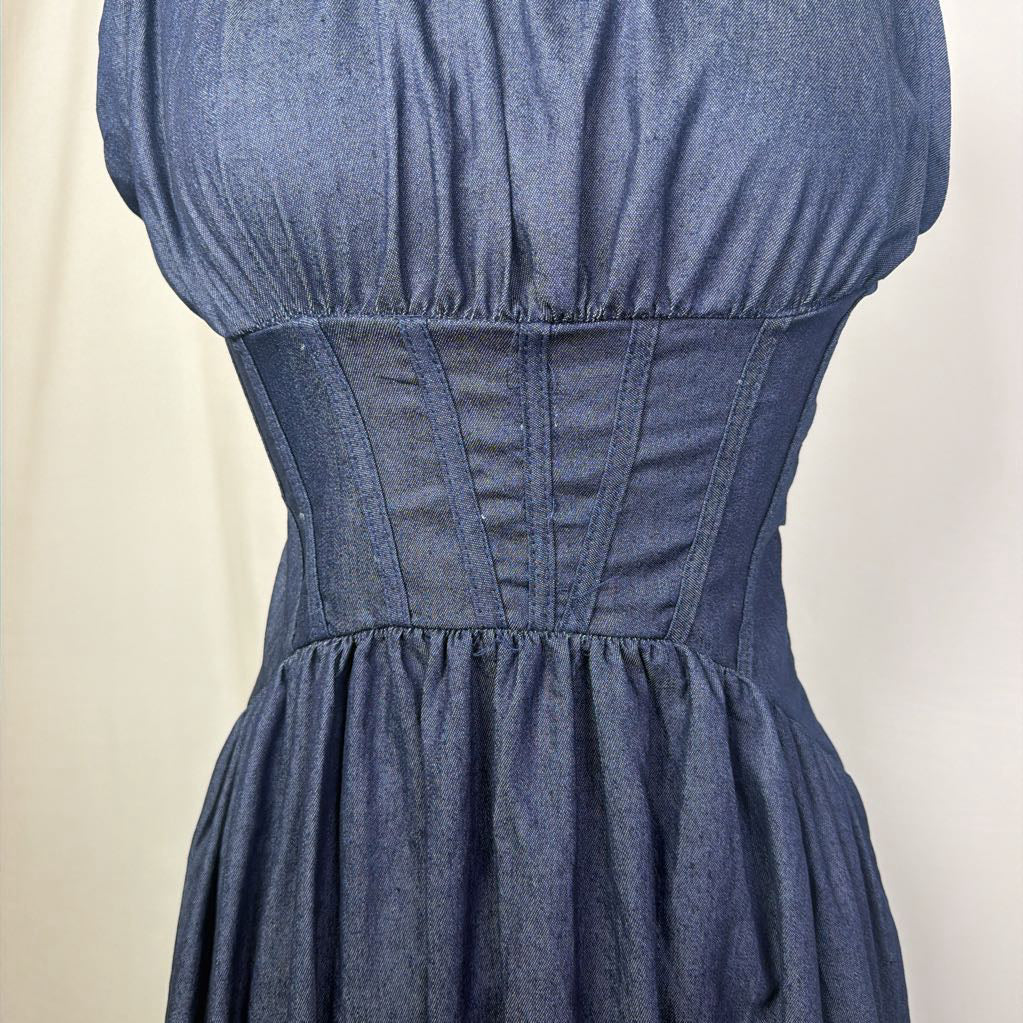 A close-up of a blue denim dress with a fitted corset-style waist and gathered bust, shown on a mannequin against a plain light background.