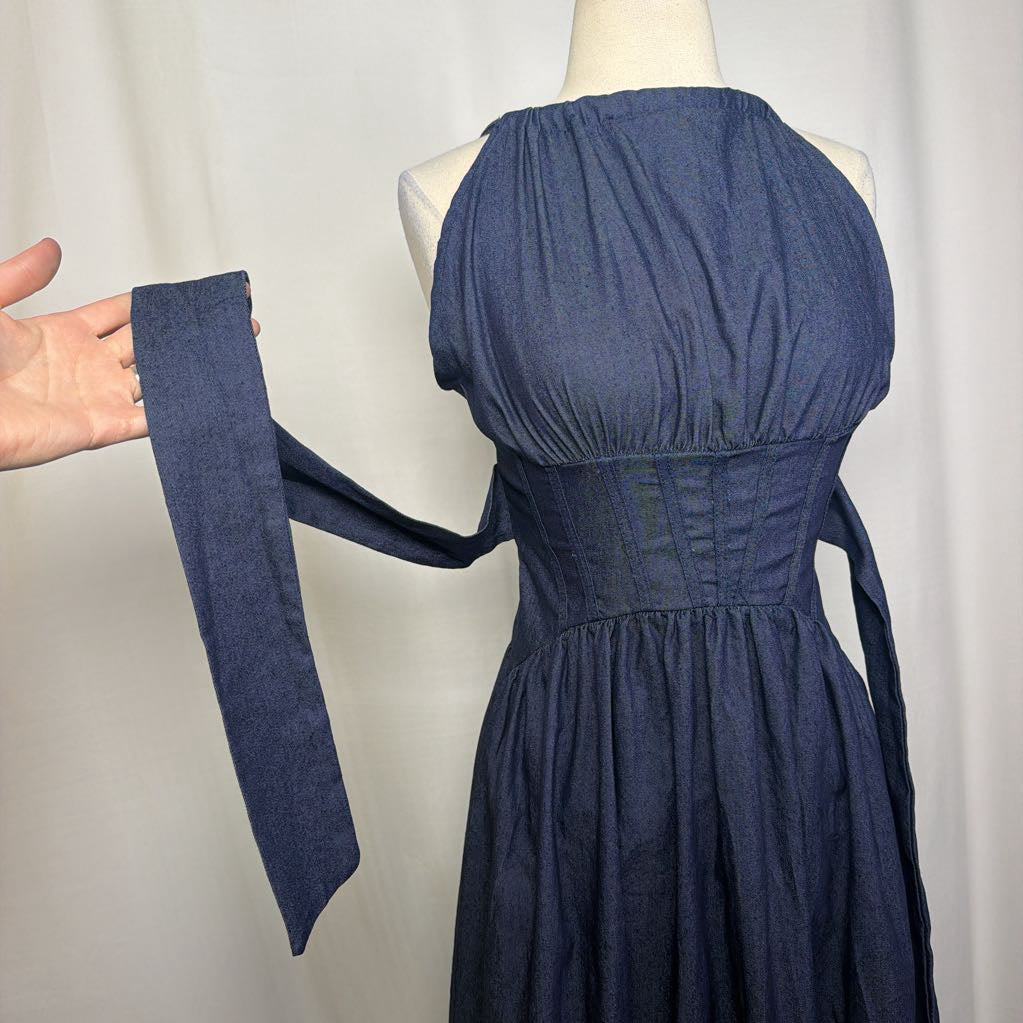 A sleeveless dark blue dress displayed on a mannequin, with a matching fabric tie or strap held out by a hand against a plain light background.