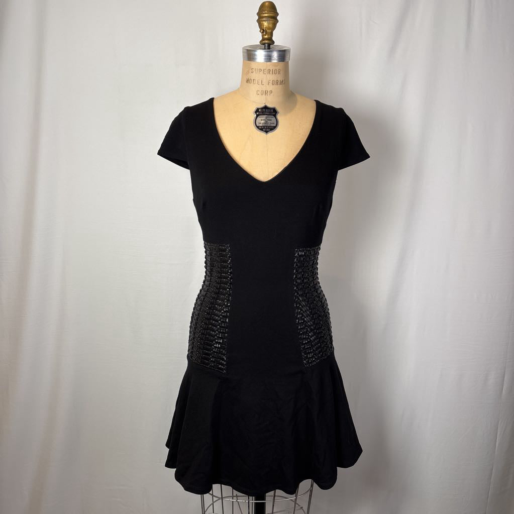 A black short-sleeve V-neck dress displayed on a dress form mannequin against a white fabric backdrop. The dress features textured, beaded side panels at the waist and a flared skirt.