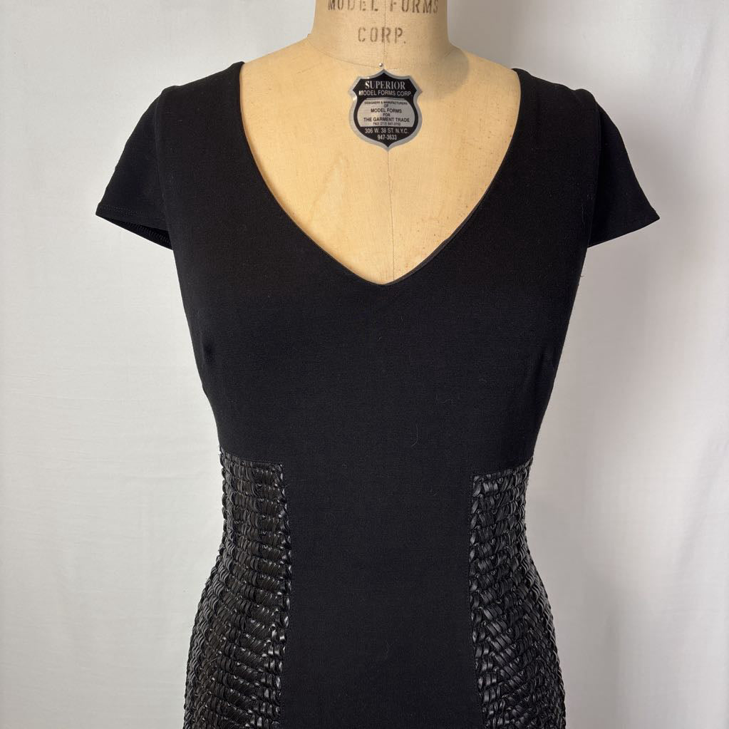 A black short-sleeve V-neck dress displayed on a beige mannequin torso against a light gray backdrop. The dress features textured, beaded paneling along the sides of the waist.